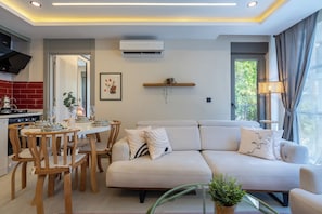 A modern living room with a sofa, dining table, chairs, and a kitchen area with a stove.