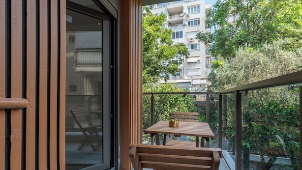A balcony with a table and chairs, a glass door, and a view of a residential building. - Botanica Houses (Muratpaşa)