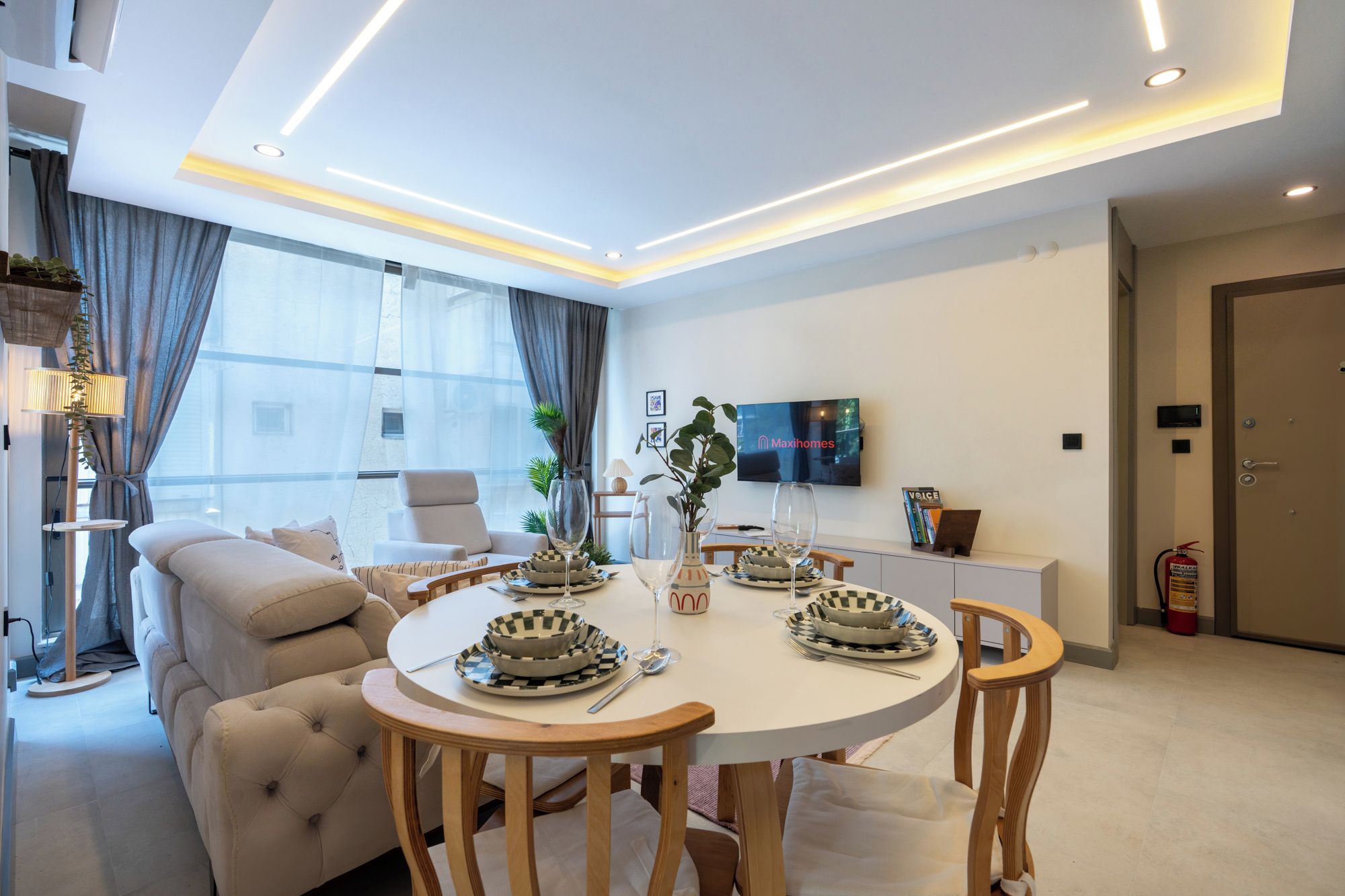 A modern living room with a round dining table, comfortable seating, a flat-screen TV, and a view of the city.