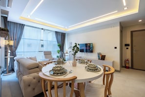 A modern living room with a round dining table, comfortable seating, a flat-screen TV, and a view of the city.