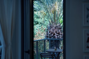 A view through a window with a table and chairs outside, surrounded by greenery.