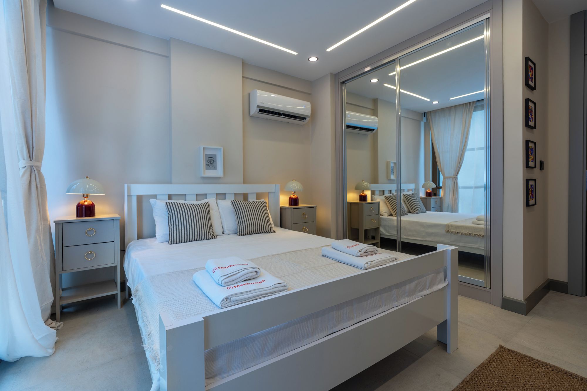A modern bedroom with a large bed, bedside tables, a mirror, and an air conditioning unit.