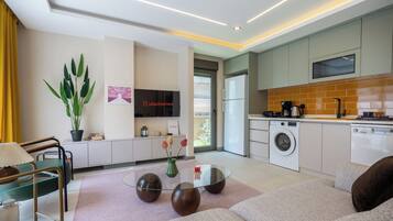 A modern living room with a glass coffee table, sofas, a TV, and a potted plant.