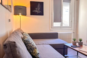 Een moderne woonkamer met een bank, een lamp, een lijst met een kunstwerk, een raam en een radiator.