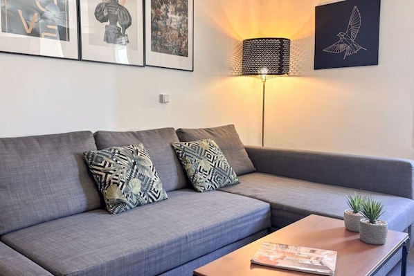 Een moderne woonkamer met een grijze bank, gestreepte kussens, een vloerlamp en een ingelijst kunstwerk aan de muur.