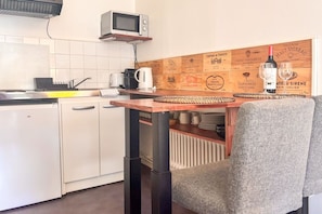 Een compacte keuken met witte kastjes, een magnetron, een koffiezetapparaat en een fles wijn op het aanrecht.