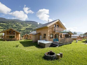 A wooden chalet with a balcony, a hot tub, and a grassy yard. - One-bedroom Cabin (Sankt Georgen am Kreischberg)