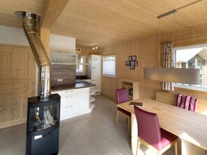 A modern kitchen with a wood stove, white cabinets, and a dining area with a table and chairs. - One-bedroom Cabin (Sankt Georgen am Kreischberg)