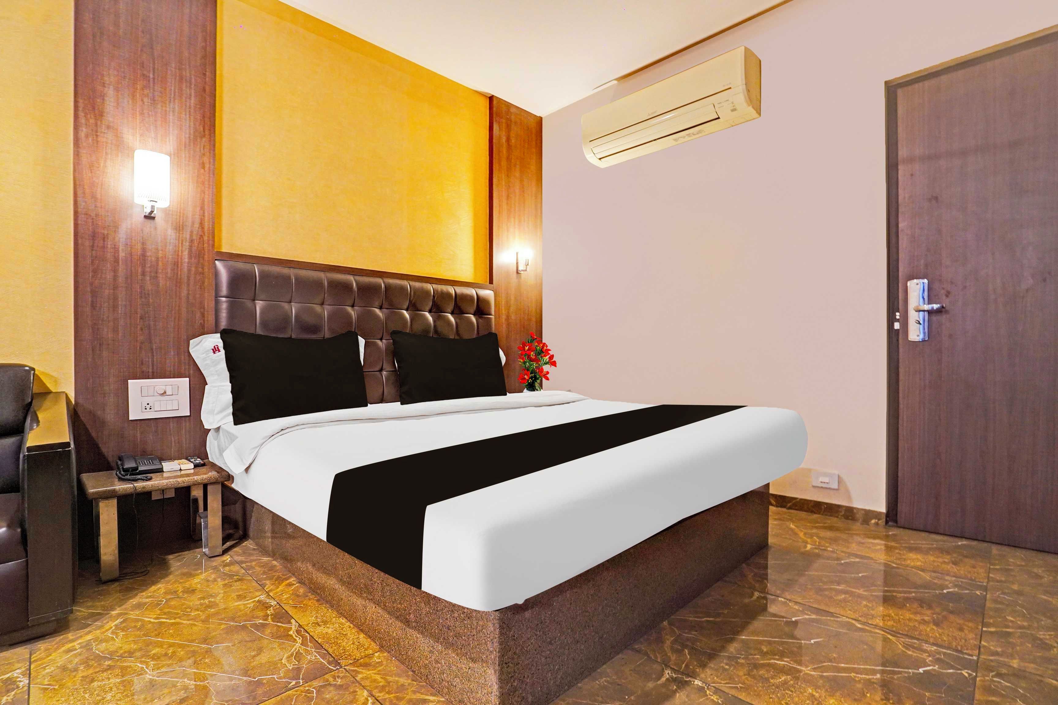 Una habitación de hotel con cama, mesita de noche, lámpara y equipo de aire acondicionado.