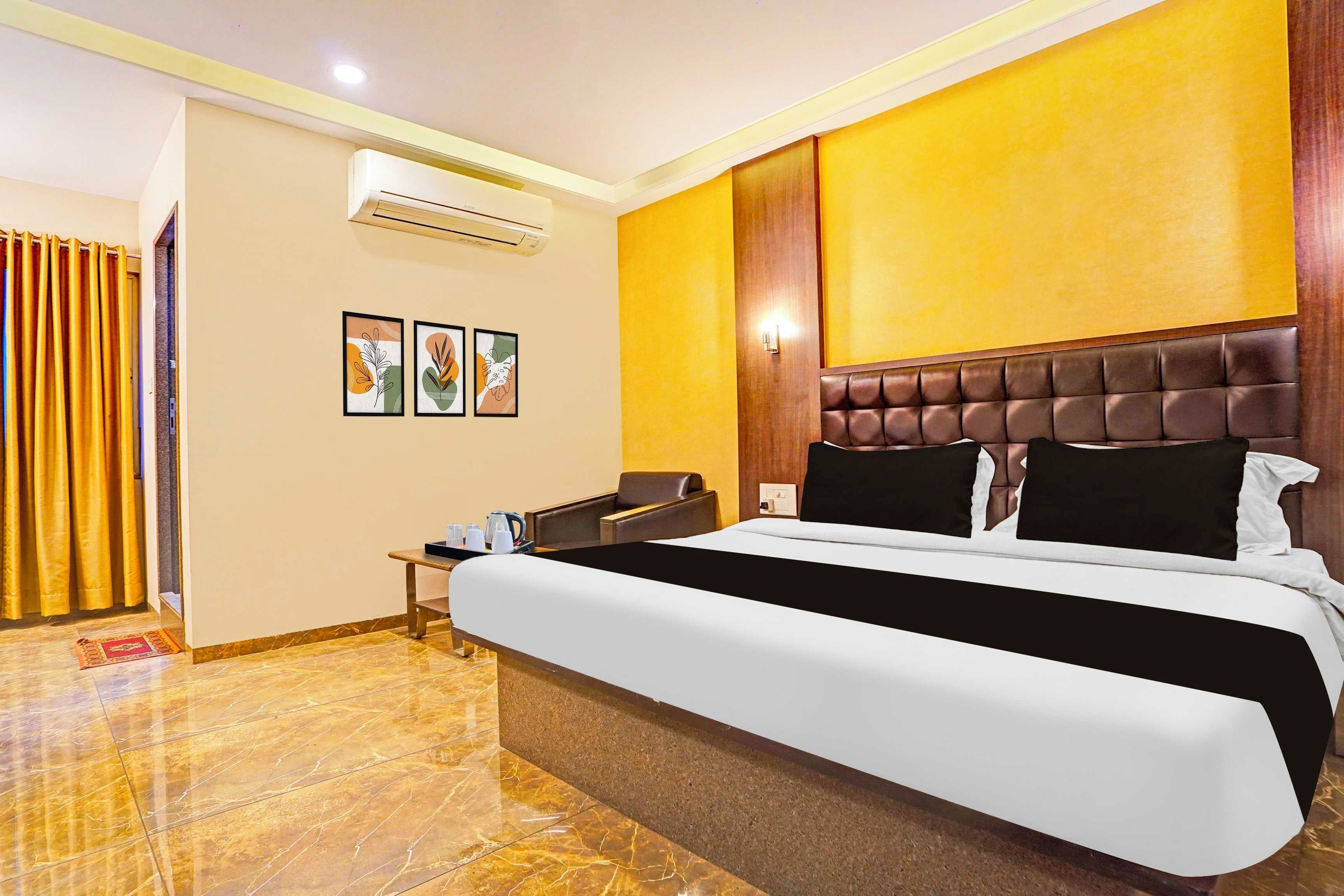 Una habitación de hotel con una cama grande, cabecero de madera, una mesita con hervidor y aire acondicionado de pared.