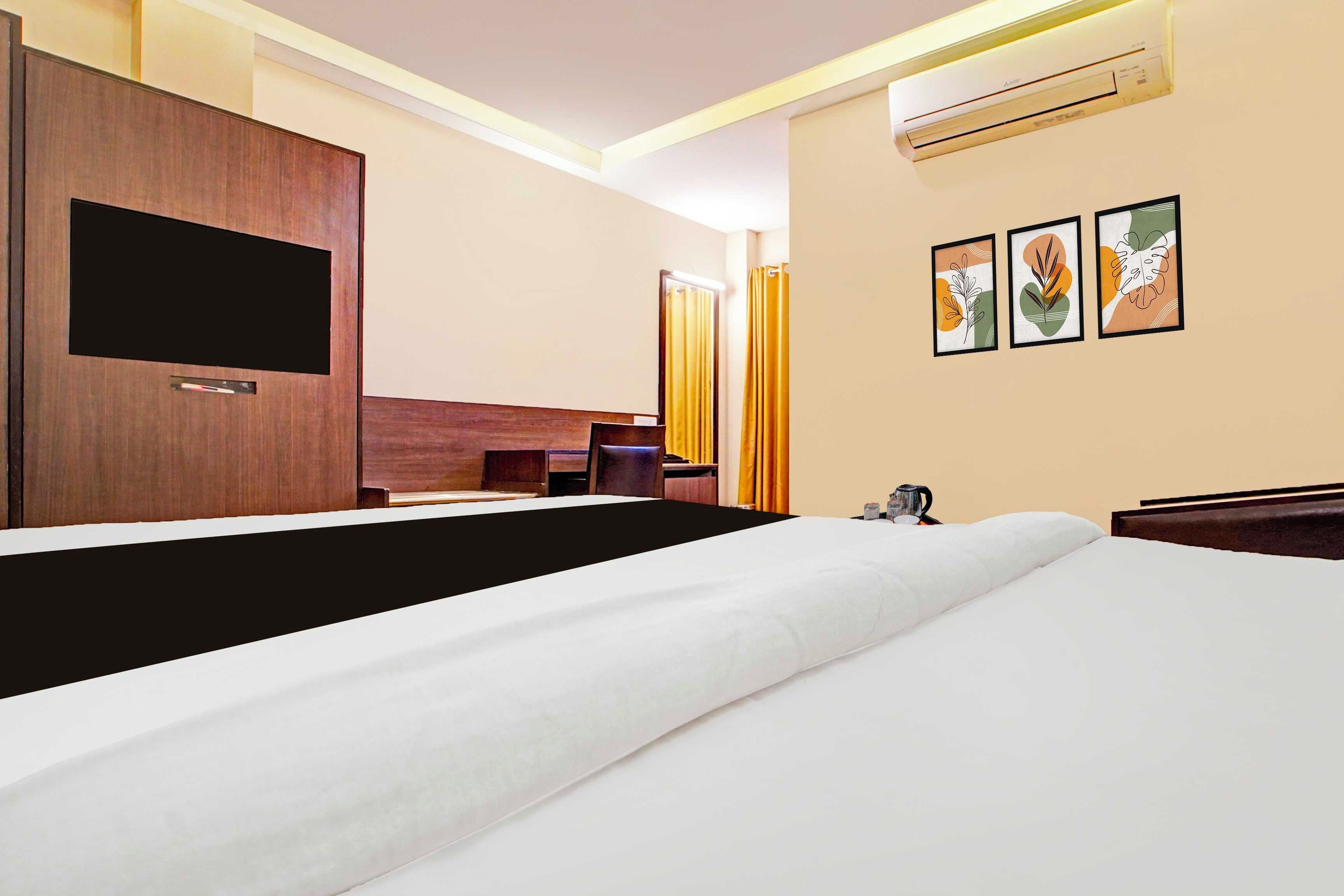 Ein Hotelzimmer mit einem Bett, einem Flachbildfernseher, einem Schreibtisch, einem Sessel, einer Klimaanlage und Bildern an der Wand.