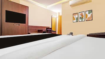 Ein Hotelzimmer mit einem Bett, einem Flachbildfernseher, einem Schreibtisch, einem Sessel, einer Klimaanlage und Bildern an der Wand.