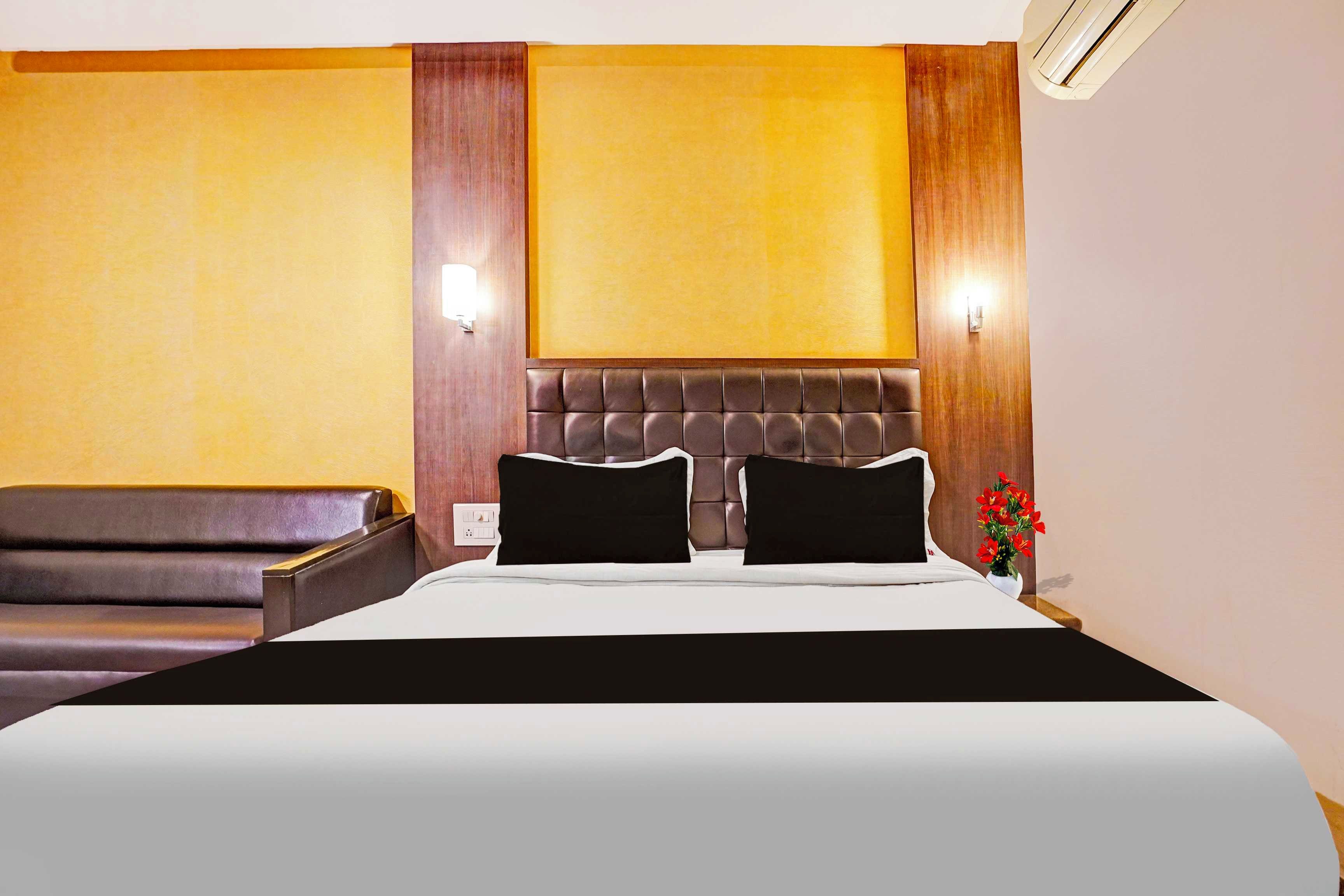 Una habitación de hotel con una cama grande, un sofá de cuero oscuro y un aire acondicionado instalado en la pared.