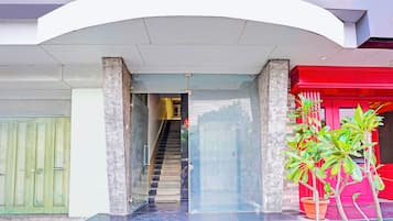 Une entrée d’immeuble avec une porte en verre, un escalier menant à l’intérieur et une structure rouge sur la droite.