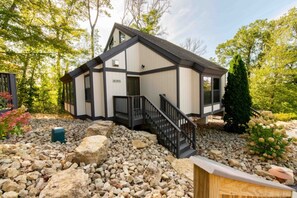 A modern two-story house with a stone foundation, a wooden deck, and a staircase leading to the entrance. - Wisconsin Dells | Couples' Leisure Stay | Pools + Golf (Wisconsin Dells)