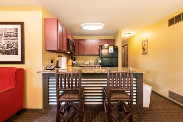 A compact kitchen with a central island, two bar stools, and a red chair.