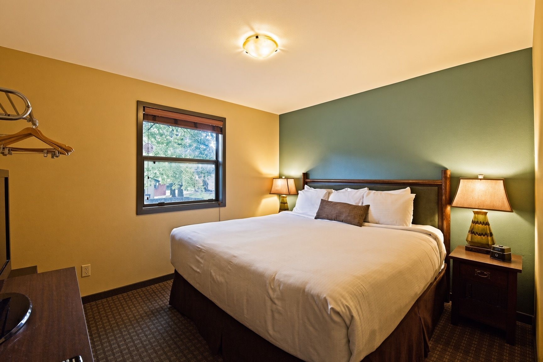 Une chambre d’hôtel avec un lit, des lampes de chevet, une fenêtre et un porte-manteau.