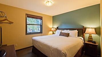 Une chambre d’hôtel avec un lit, des lampes de chevet, une fenêtre et un porte-manteau.