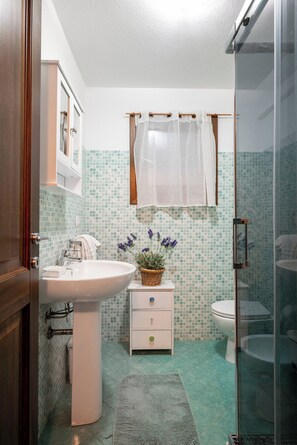 Et badeværelse med en hvid vask, toilet, brusebad og en flisebeklædt væg.