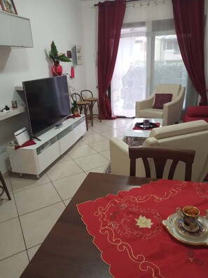 A living room with a flat-screen TV, a sofa, a coffee table with a red table runner, and a dining table with a teapot and cup. - A Splendid Home at Olbia (Olbia)