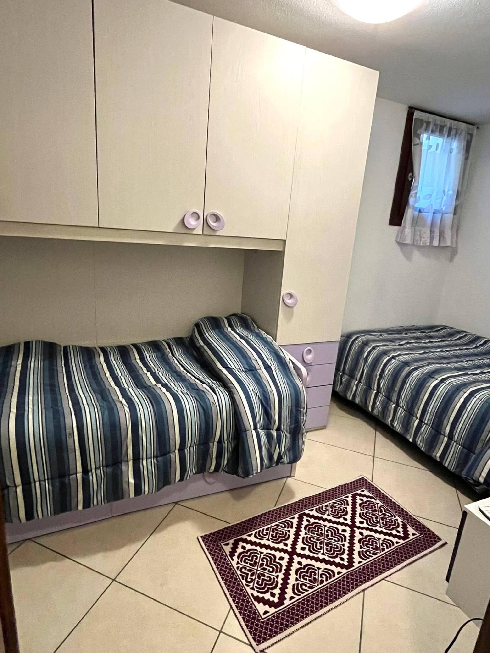 A small room with two beds, a window with curtains, and a patterned rug.