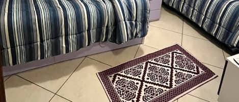 A small room with two beds, a window with curtains, and a patterned rug.