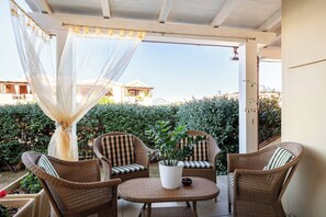 An outdoor patio with wicker furniture, a white pot with plants, and a view of a building and greenery in the background. - A Splendid Home at Olbia (Olbia)