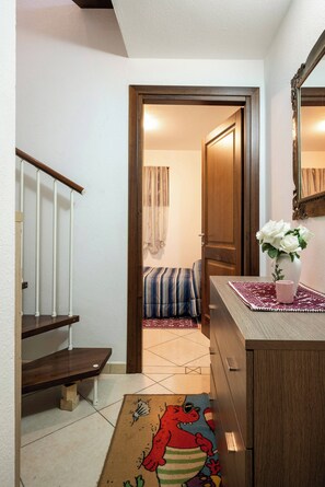 A hallway with a wooden staircase, a striped sofa, a wooden door, and a vase with white flowers on a table. - A Splendid Home at Olbia (Olbia)