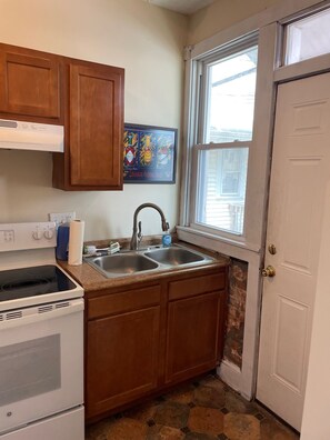 A kitchen with wooden cabinets, a stainless steel sink, a stove, and a window with a view of the outside.