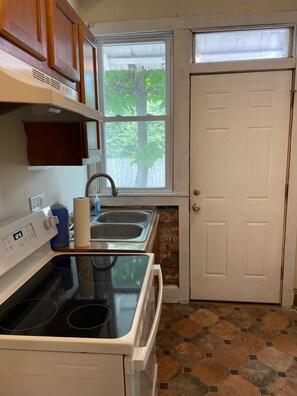 A kitchen with a stove, sink, and window overlooking a tree.