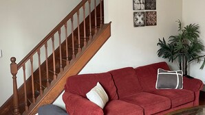 Una sala de estar con un sofá rojo, una escalera de madera y una mesa de centro de vidrio.