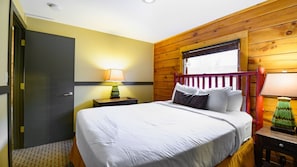 A bedroom with a bed, a nightstand, a lamp, and a window with a view.