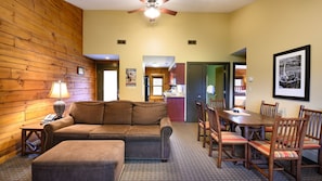 A cozy room with a wooden wall, a sofa, a dining table with chairs, and a ceiling fan.