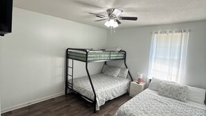 A bedroom with a bunk bed, a single bed, a ceiling fan, a window with curtains, and a TV mounted on the wall. - Soft Haven/ Warm and Cozy Getaway (Clarksville)