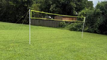 Ein grasbewachsenes Feld mit einer gelben Netzkonstruktion, möglicherweise für Sportzwecke, umgeben von Bäumen und einem Holzzaun.