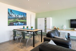 Ein modernes Wohnzimmer mit einem schwarzen Ledersofa, einem Esstisch mit Stühlen, einem Flachbildfernseher und einem Gemälde eines Golfplatzes.