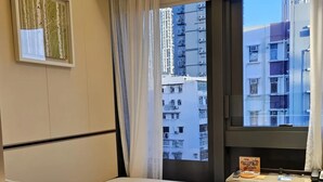 A hotel room with a bed, a desk, a chair, a window with curtains, and a framed picture on the wall. - wangwangwang (Kwun Tong)