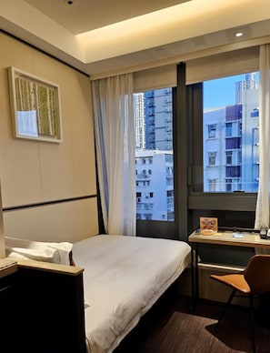 Habitación de hotel con cama, escritorio, silla, ventana con cortinas e imagen enmarcada en la pared.