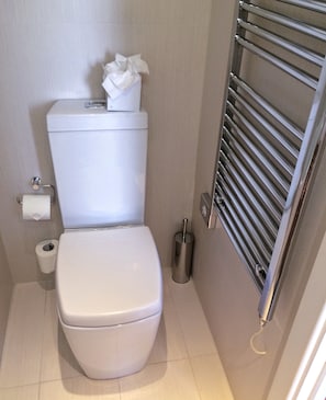 Un baño pequeño con inodoro blanco, un dispensador de toallas de papel y un bidé de metal.