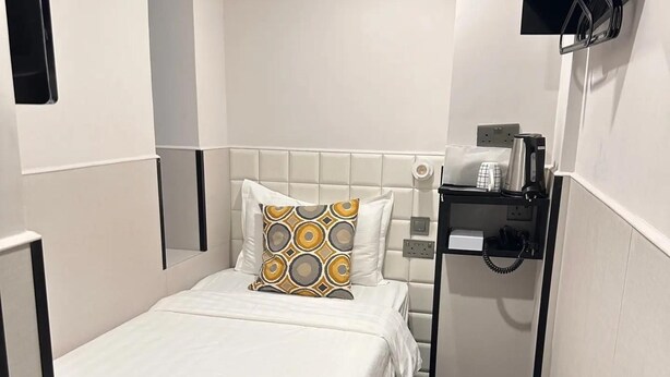 A small, compact hotel room with a single bed, a bedside table with a phone, and a wall-mounted TV. - wangwangwang (Kwun Tong)