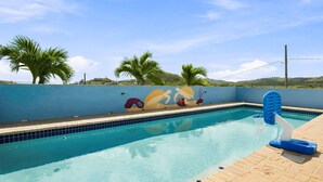 Ein Swimmingpool mit Wandmalerei, Palmen und blauem Himmel.
