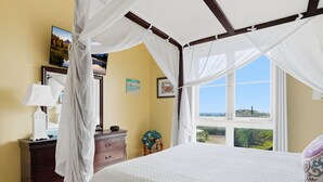 Ein Schlafzimmer mit Baldachinbett, Kommode, Lampe und Blick ins Freie.