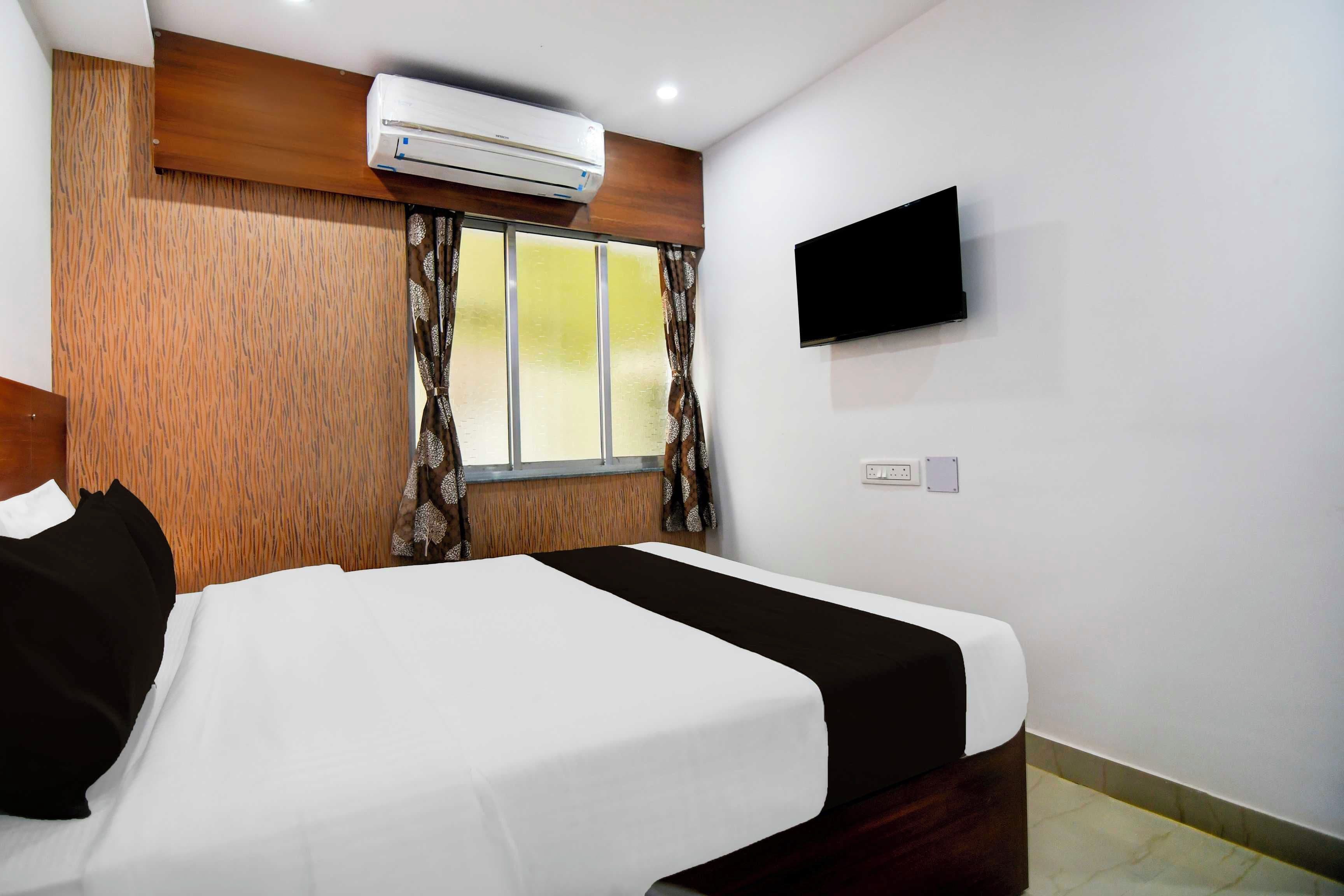 Habitación de hotel con cama, televisión de pantalla plana montada en la pared y equipo de aire acondicionado sobre la cama.