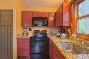 A kitchen with a granite countertop, stainless steel sink, and red cabinets. - Wisconsin Dells | Waterpark Launchpad | Pools + Golf | 2BR (Wisconsin Dells)