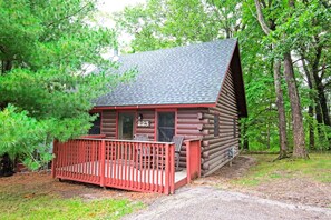 A log cabin with a porch, numbered 223, surrounded by trees. - Wisconsin Dells | Waterpark Launchpad | Pools + Golf | 2BR (Wisconsin Dells)
