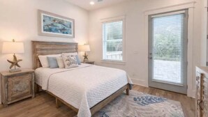 A bedroom with a bed, nightstands, a ceiling fan, a window with blinds, and a door. - NEW: Saltwater Sky - Rooftop deck and private pool (Eastpoint)