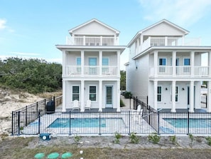 Ein Strandhaus mit zwei Etagen, einem Swimmingpool, einer überdachten Terrasse und einem umzäunten Deckbereich.