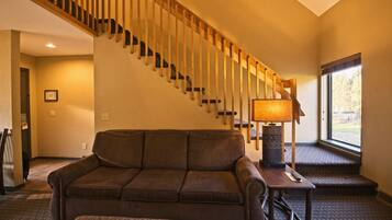 A living room with a brown sofa, a wooden staircase, a lamp, and a window with a view.