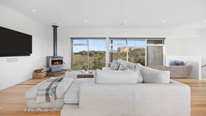 A modern living room with a large sofa, a fireplace, and large windows offering a view of the outdoors. - Saltaire - stunning 4 bedroom property with indoor pool (St Andrews Beach)