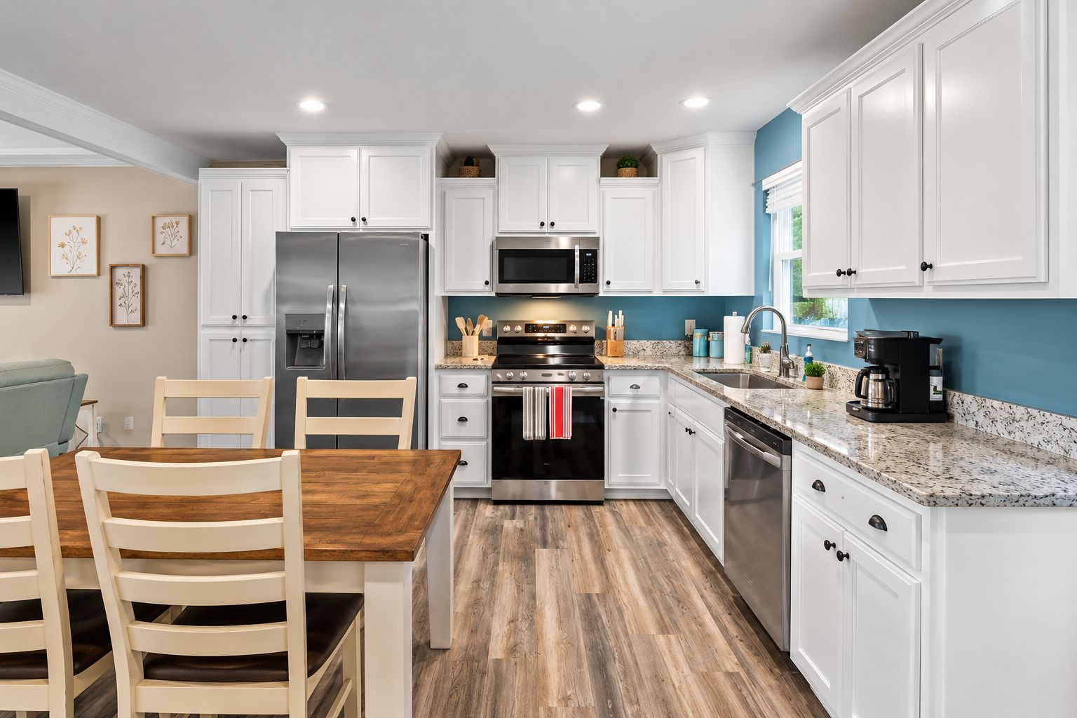 Una cocina moderna con armarios blancos, electrodomésticos de acero inoxidable, una mesa de comedor de madera y una pared de acento azul.